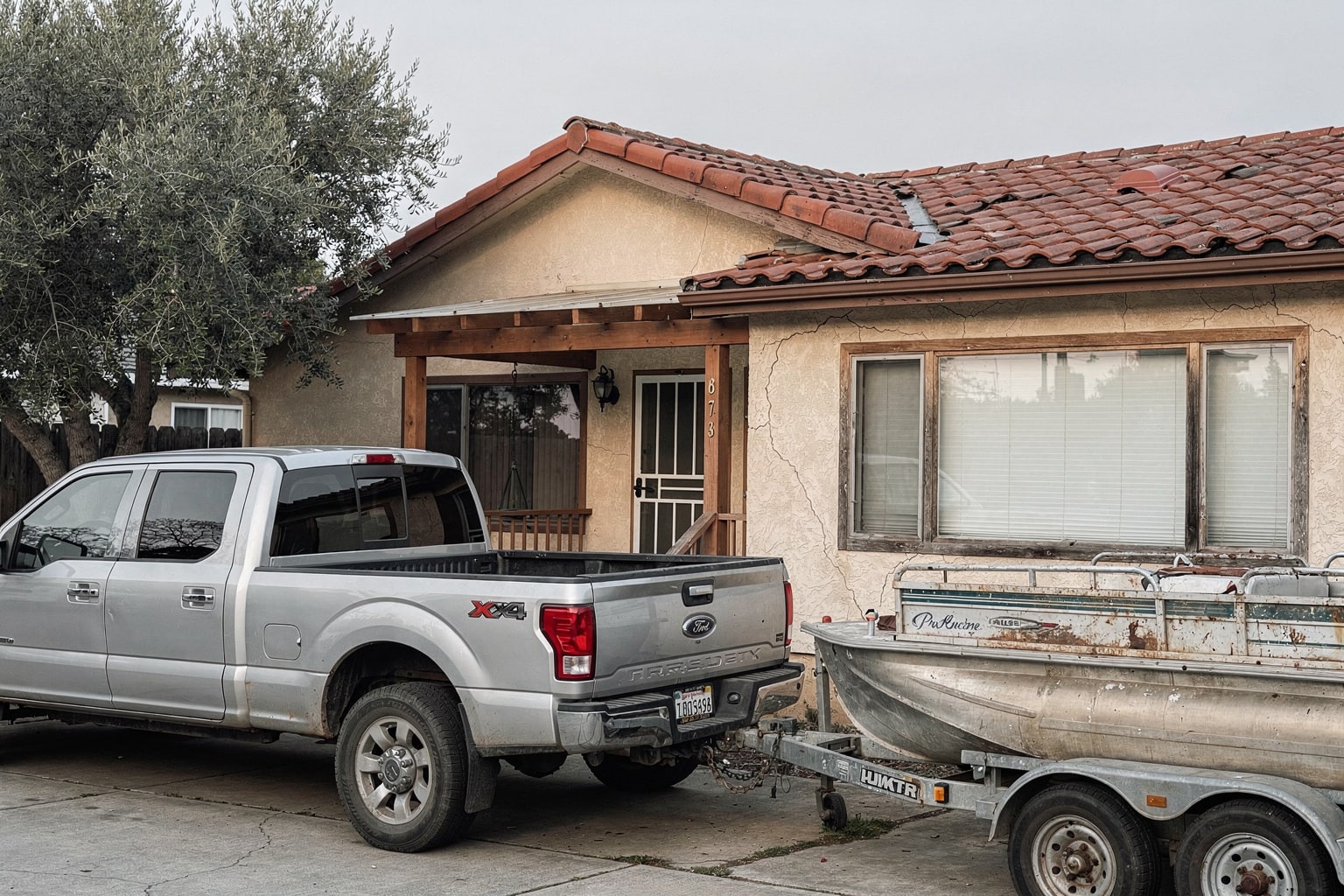 Junk boat removal San Jose showing abandoned pontoon boat surrounded by weeds with pickup truck and trailer ready for disposal