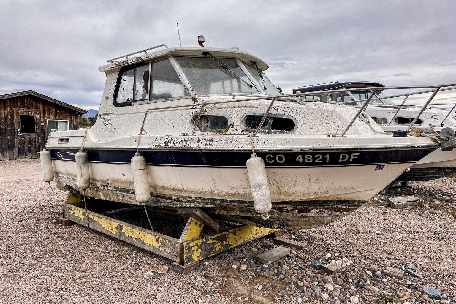Damaged junk boat on wooden cradle in Colorado Springs storage yard ready for boat disposal