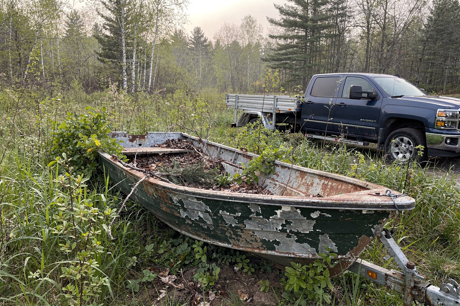Abandoned weathered aluminum jon boat in overgrown Vermont backyard ready for junk removal