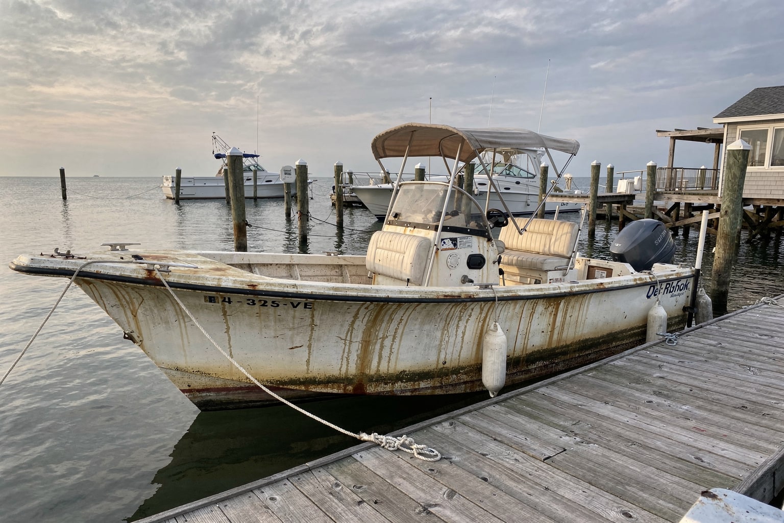 Neglected 22-foot center console boat moored at Virginia Beach marina dock showing algae and weathering