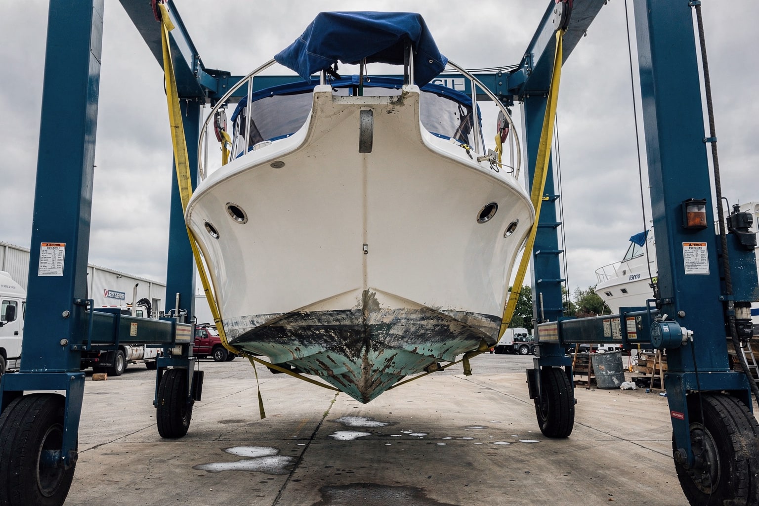 28-foot cabin cruiser suspended in travel-lift slings at DC industrial boat salvage facility, full hull exposure