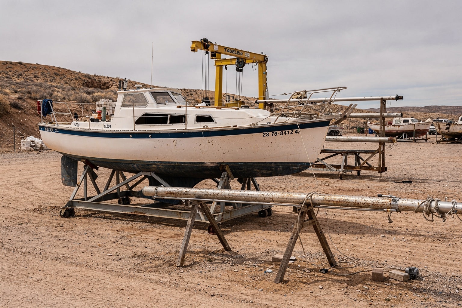 Large sailboat on steel cradle at New Mexico marine salvage yard with travel-lift equipment visible