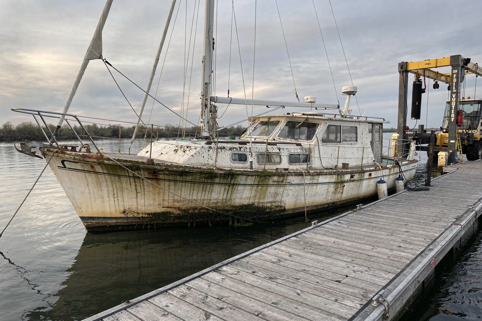 Stained 28-foot sailboat moored at Idaho marina dock with travel-lift staged for marine salvage boat removal service