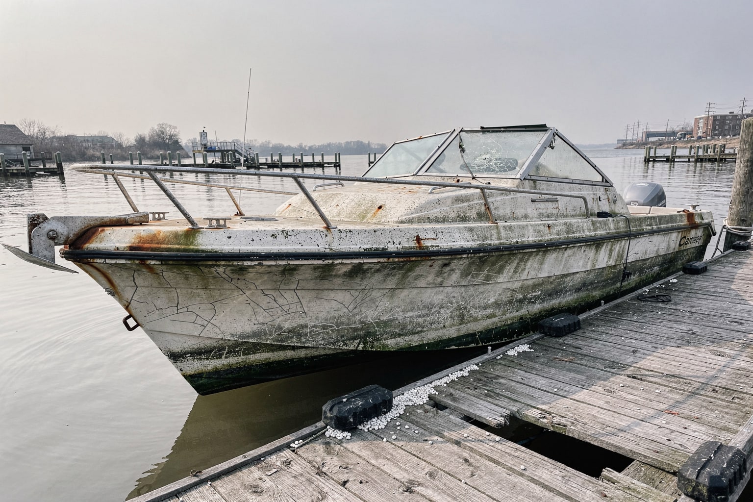 Abandoned 22-foot center console powerboat with algae growth moored at weathered DC marina pier, surrounded by neglected vessels